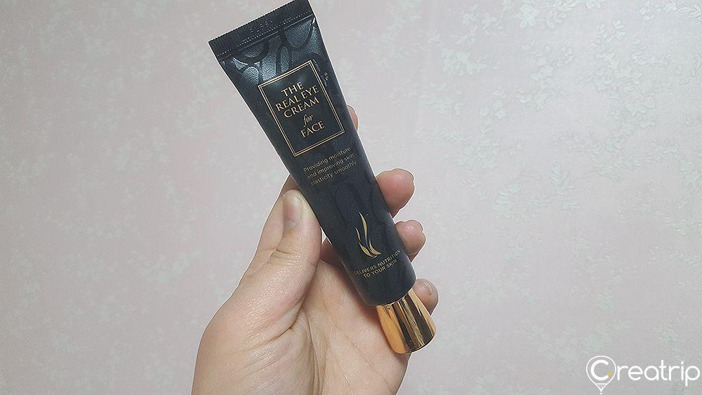 Hand holding AHC The Real Eye Cream for Face showcasing how to apply this multi-purpose skincare product.